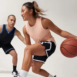 Vrouw die een basketbal dribbelt terwijl een man in verdedigende houding haar verdedigt tegen een effen lichte achtergrond.
