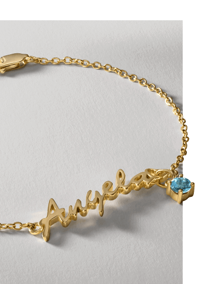 A gold bracelet reading ‘Angela’ with a blue gemstone. 