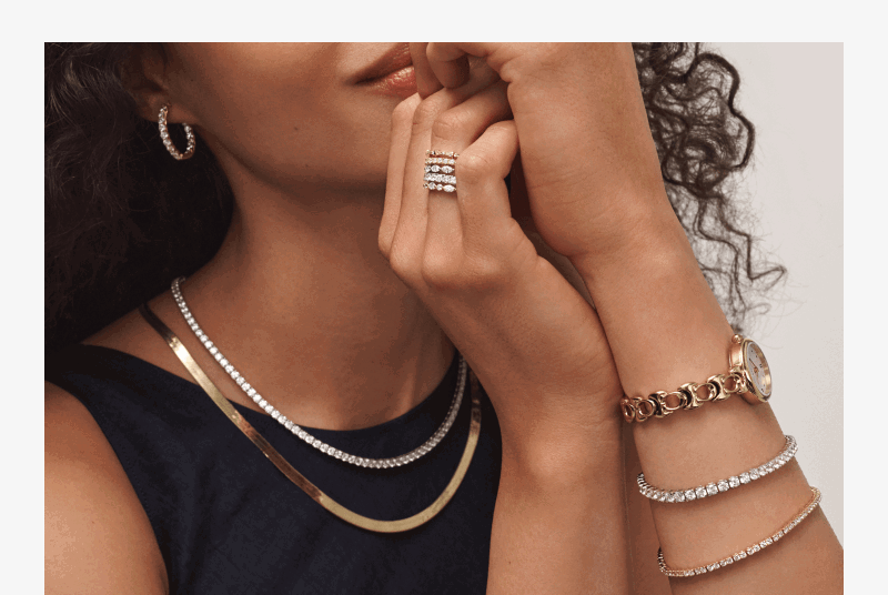 A woman wearing layered necklaces in silver and gold. Matching tennis bracelets, a gold watch, diamond hoops and a stack of earrings. 