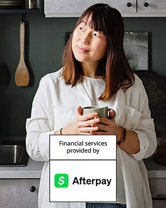 A women standing in her kitchen, holding a coffee cub. The Afterpay logo overlays the image.
