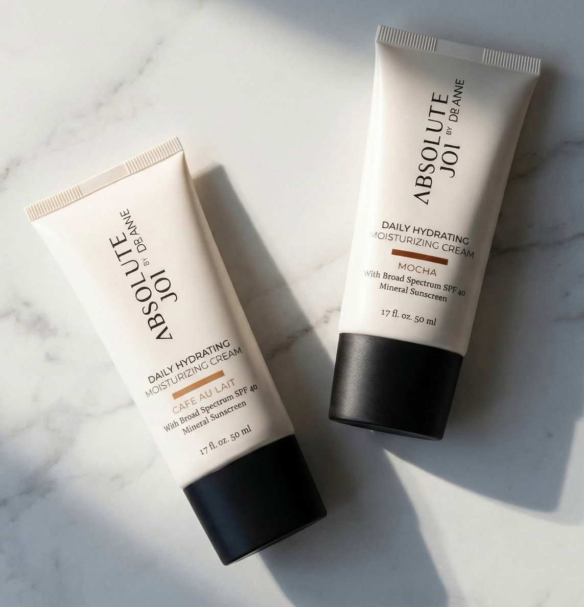 Two bottles of Cafe Au Lait and Mocha Tinted Moisturizers on Marble table.