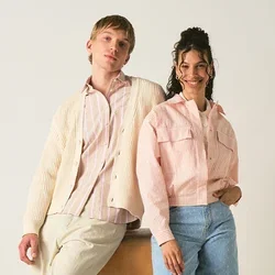 Twee jonge volwassenen in casual pastelkleding poseren, één leunt op een houten turnkast, tegen een egale lichte achtergrond.