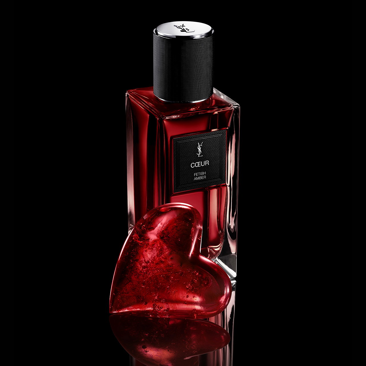 A bottle of YSL Coeur Eau de Parfum standing behind a glowing, red crystalline heart-shaped sculpture on a black background.