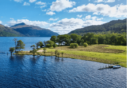 Scenic view of a tranquil lake surrounded by lush greenery and mountains under a blue sky.