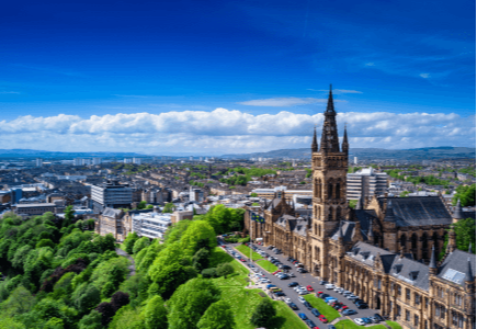 Aerial view of a cityscape featuring a historic building, lush greenery, and a clear blue sky.