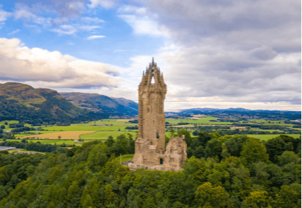 A tall stone tower surrounded by lush greenery and rolling hills under a cloudy sky.