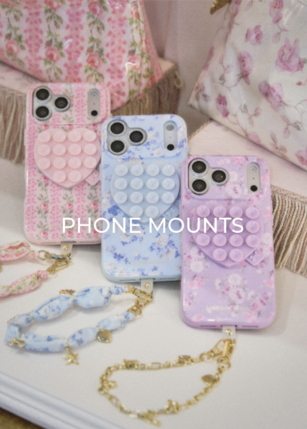 Three phones dressed in the Case-Mate x LoveShackFancy phones cases and matching accessories.