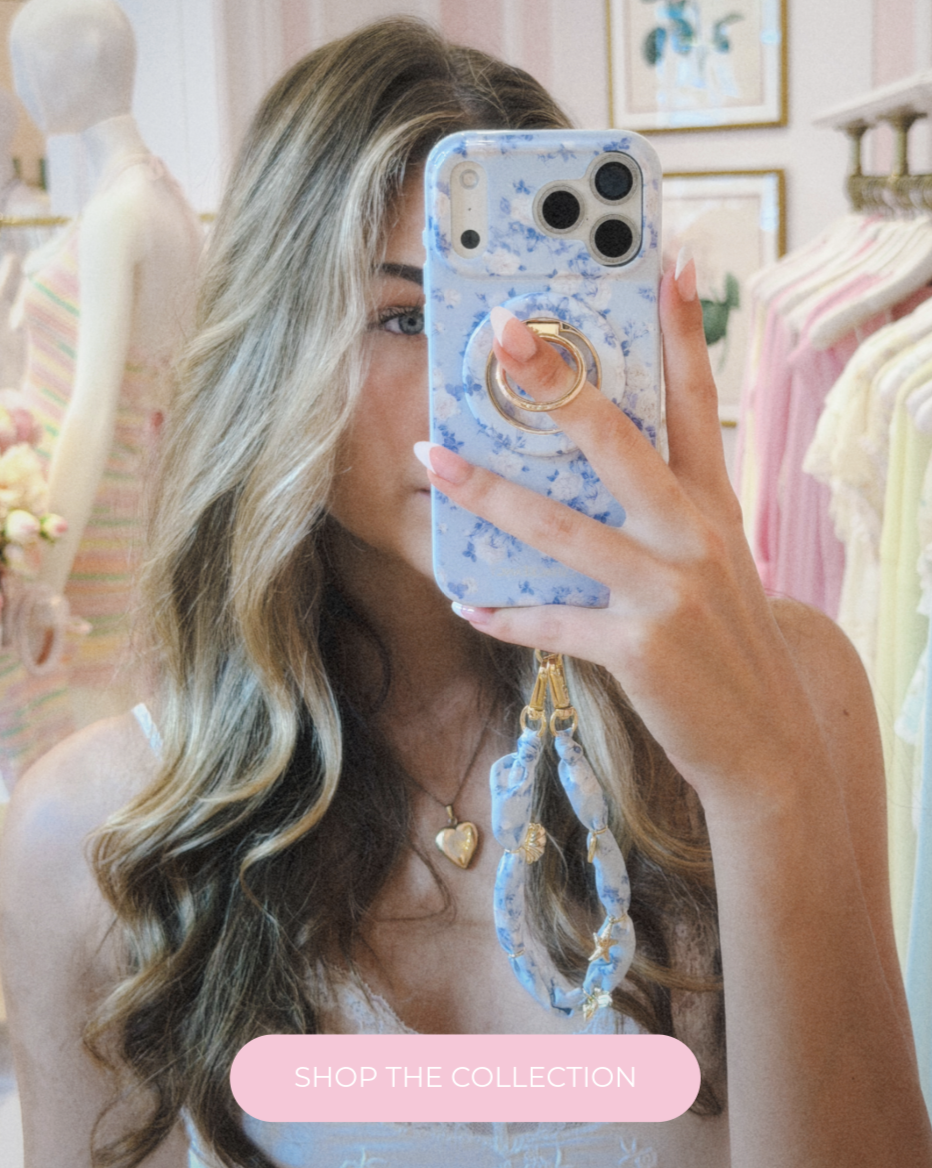 A girl taking a mirror selfie to show off her Case-Mate x LoveShackFancy Everblooming Rosettes phone case, ring stand and scarf phone charm.