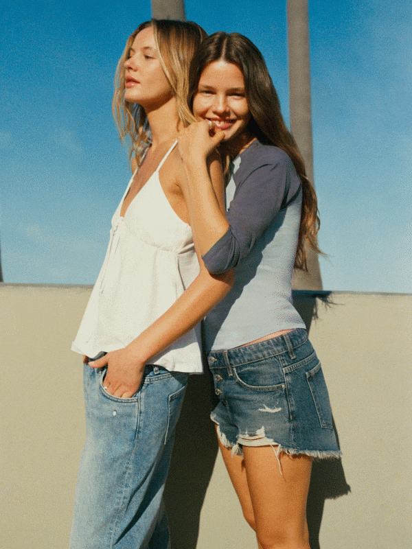Two women wearing casual denim and tops against blue sky background