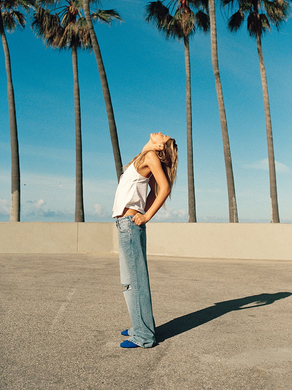 Woman in white tank top and light blue jeans posing outdoors