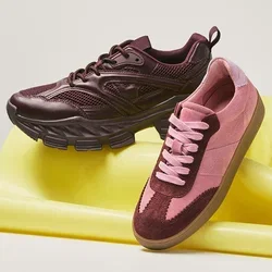 Een paar bordeauxrode en roze sneakers die rusten op een opgevouwde gele fitnessmat tegen een effen achtergrond.