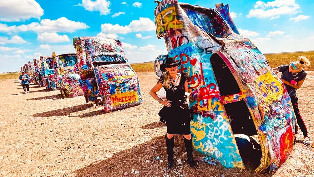 Image description: Woman posing for photo at Cadillac Ranch, outside of Amarillo, Texas on old Route 66.
