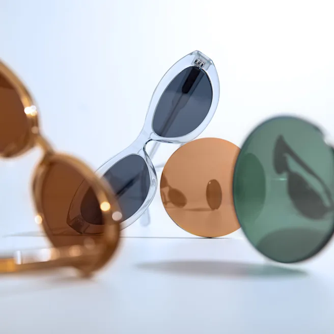 12:49 Sonnenbrille mit transparentem Rahmen zwischen verschiedenen getönten Gläsern in Braun, Orange und Grün.