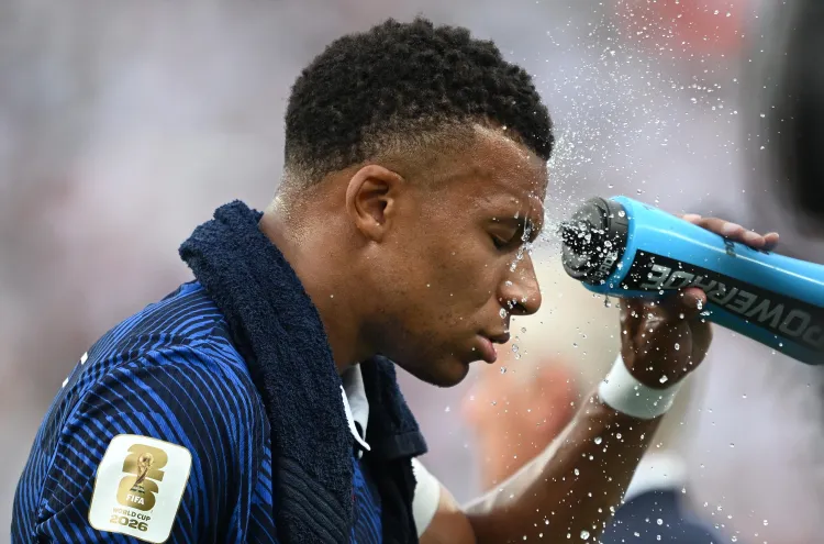 Kylian Mbappe, a towel around his shoulders, sprays water on his face from a blue Powerade bottle.