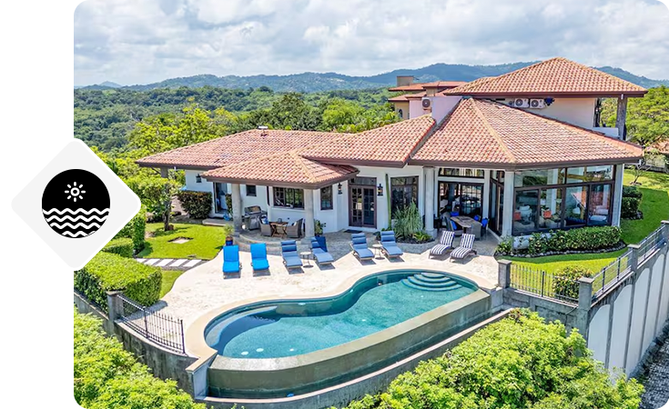 Hillside villa with tiled roof, curved pool, and patio seating overlooking the landscape.