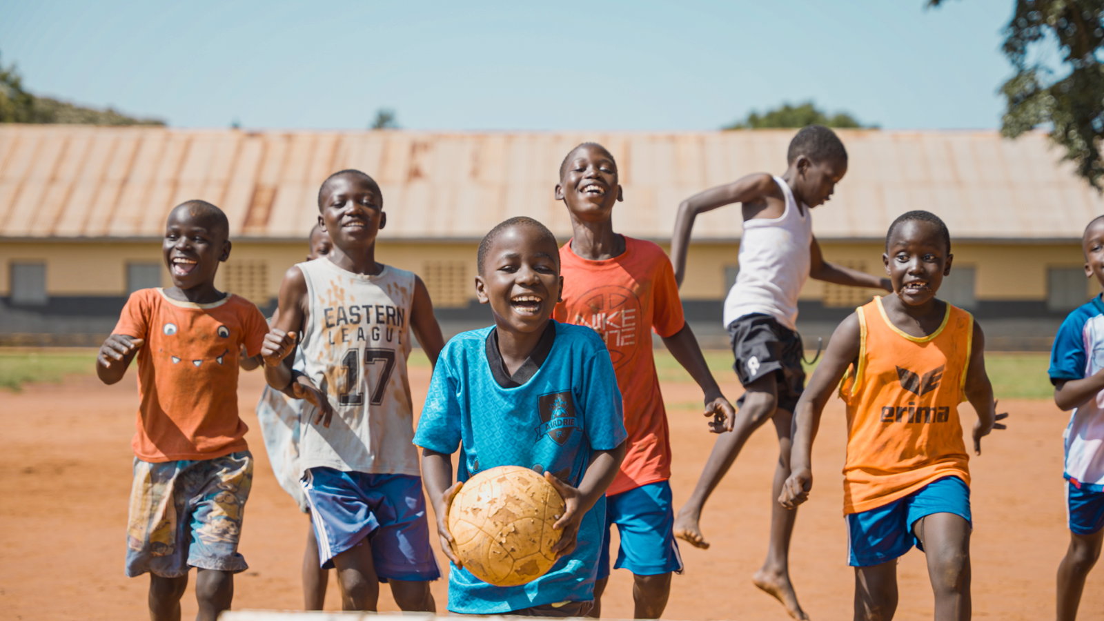A group of young boys smiling as they play football.