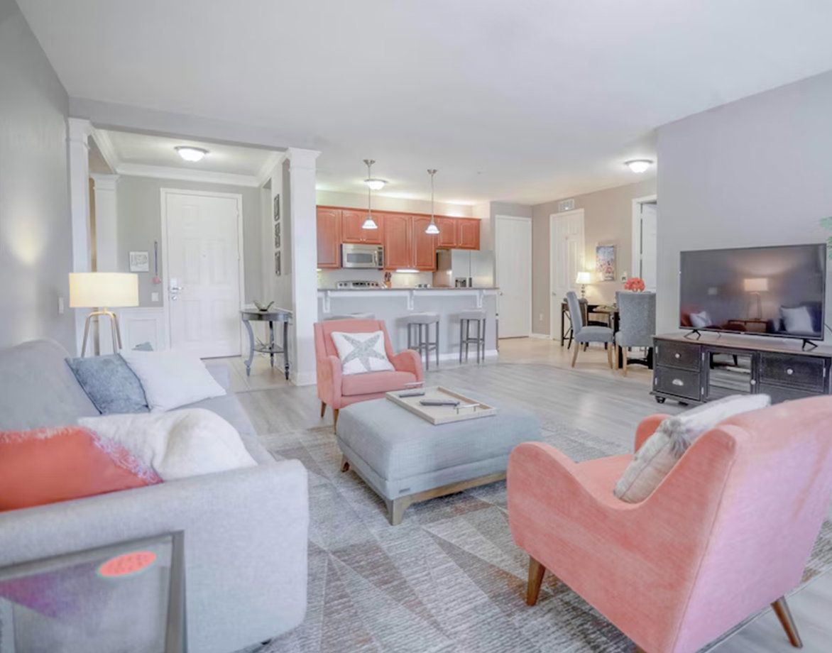 Open-plan living area with sofa, armchairs, ottoman, and kitchen with bar seating.