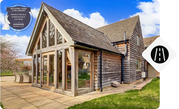 Wood-clad cottage with large windows, patio seating, and garden.
