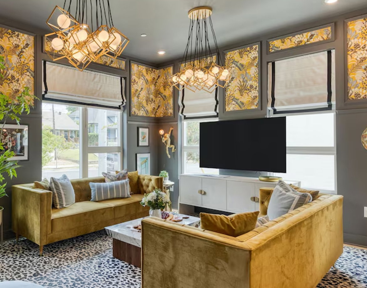 Bright living room with sofas, patterned wallpaper, modern chandeliers, and a TV on a white console.