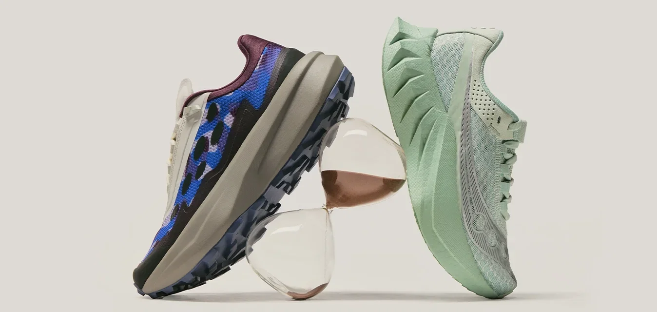Twee sportschoenen, één blauw met een camouflag patroon en één lichtgroen, in balans op gestapelde glazen voorwerpen tegen een effen achtergrond.