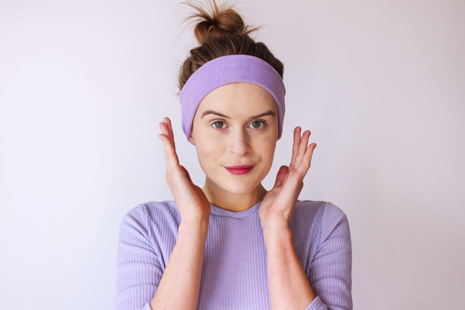 A woman wearing lavendar sleepphones headphones looking into the camera. 