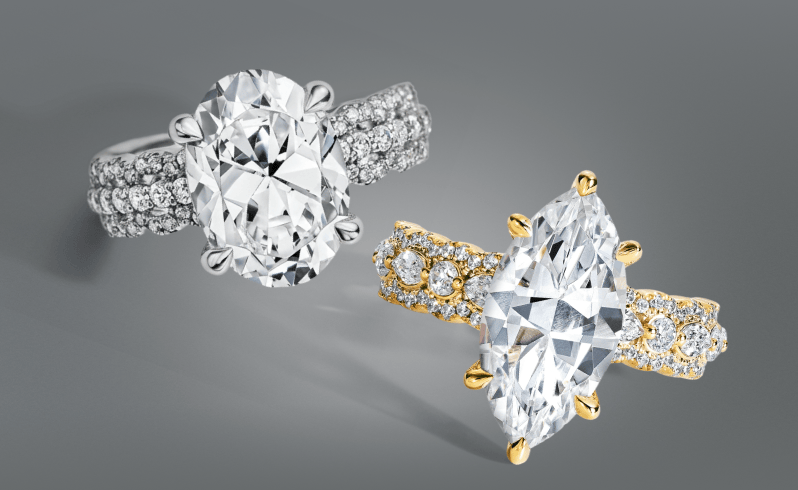 A white metal ring with an oval cut diamond next to a gold ring with a marquise cut diamond.