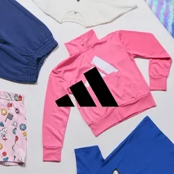 Variati articoli di abbigliamento per bambini, tra cui una giacca rosa con zip, pantaloni corti con fantasia e leggings multicolori, disposti su una superficie bianca.
