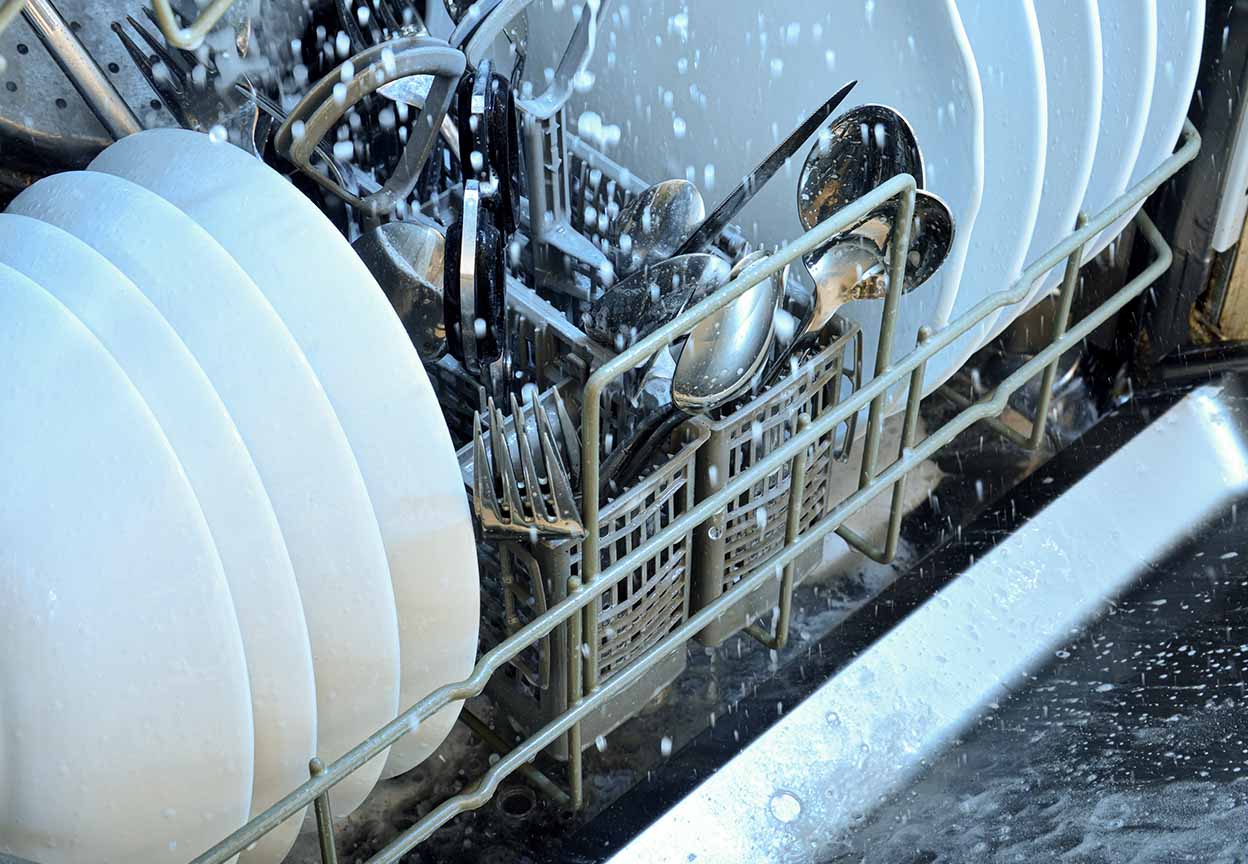 Dishwasher rack with plates and utensils being sprayed during a wash cycle