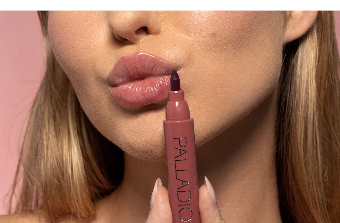 Model holding Palladio Lip Stain Marker in Blush against soft pink background.