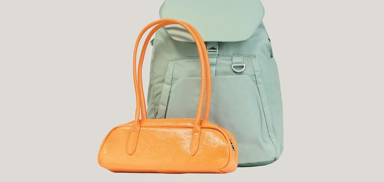 Bolso naranja brillante con asas largas frente a una mochila verde claro con solapa y bolsillos delanteros sobre un fondo liso.