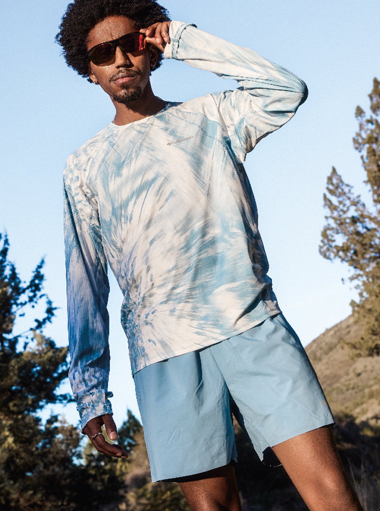 Man outside wearing Columbia long sleeve and shorts, pulling on his sunglasses.