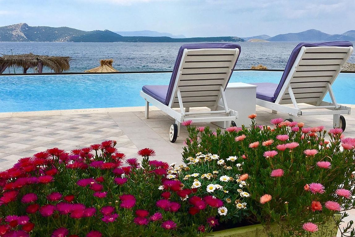 Two purple-cushioned sun loungers by an infinity pool overlooking the sea and distant islands, colourful flowers in the foreground