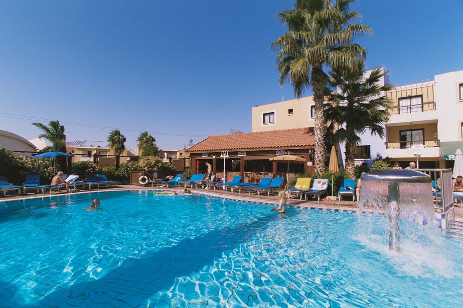 Outdoor hotel swimming pool at a sunny resort with clear blue water, palm trees, sun loungers and people enjoying the pool
