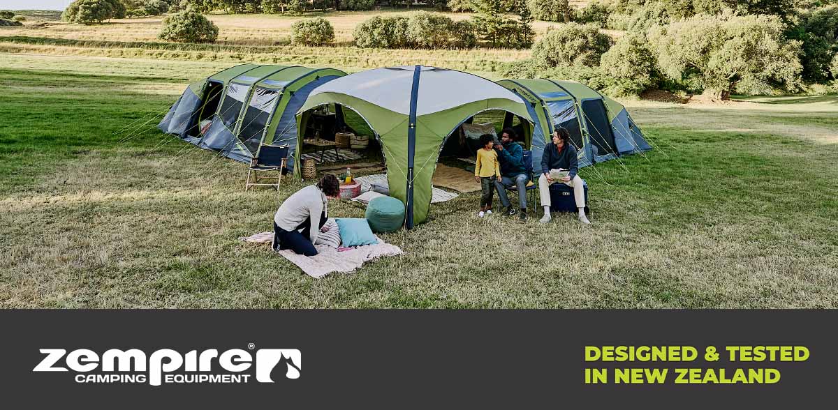 Large green family camping tent set up in an open grassy field, with people relaxing outside and a Zempire Camping Equipment promotional banner displayed below.