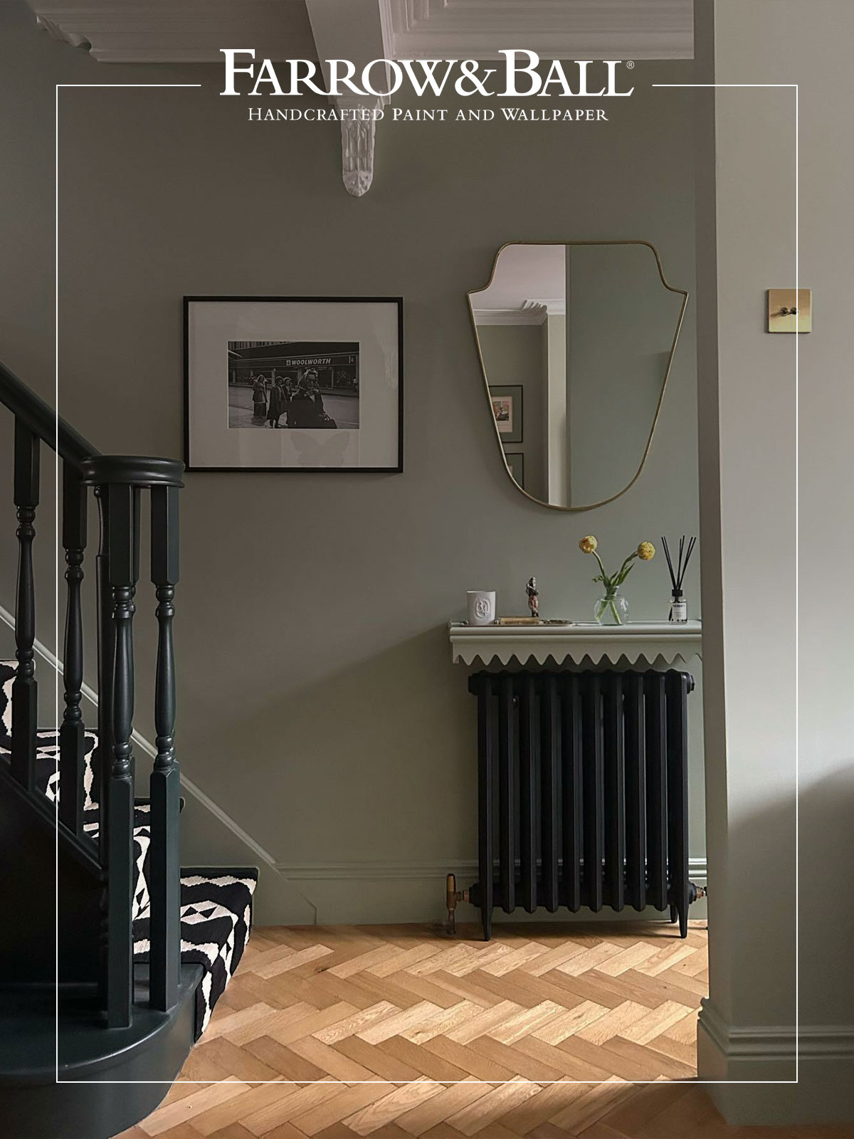 Hallway painted in soft green with a gold mirror, dark radiator, and herringbone floor.