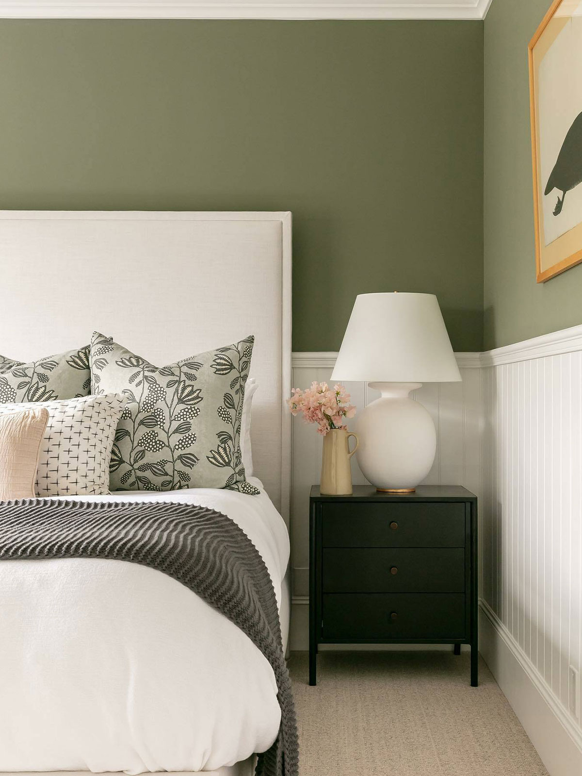 Peaceful bedroom with olive walls, white headboard, patterned cushions, and bedside lamp.