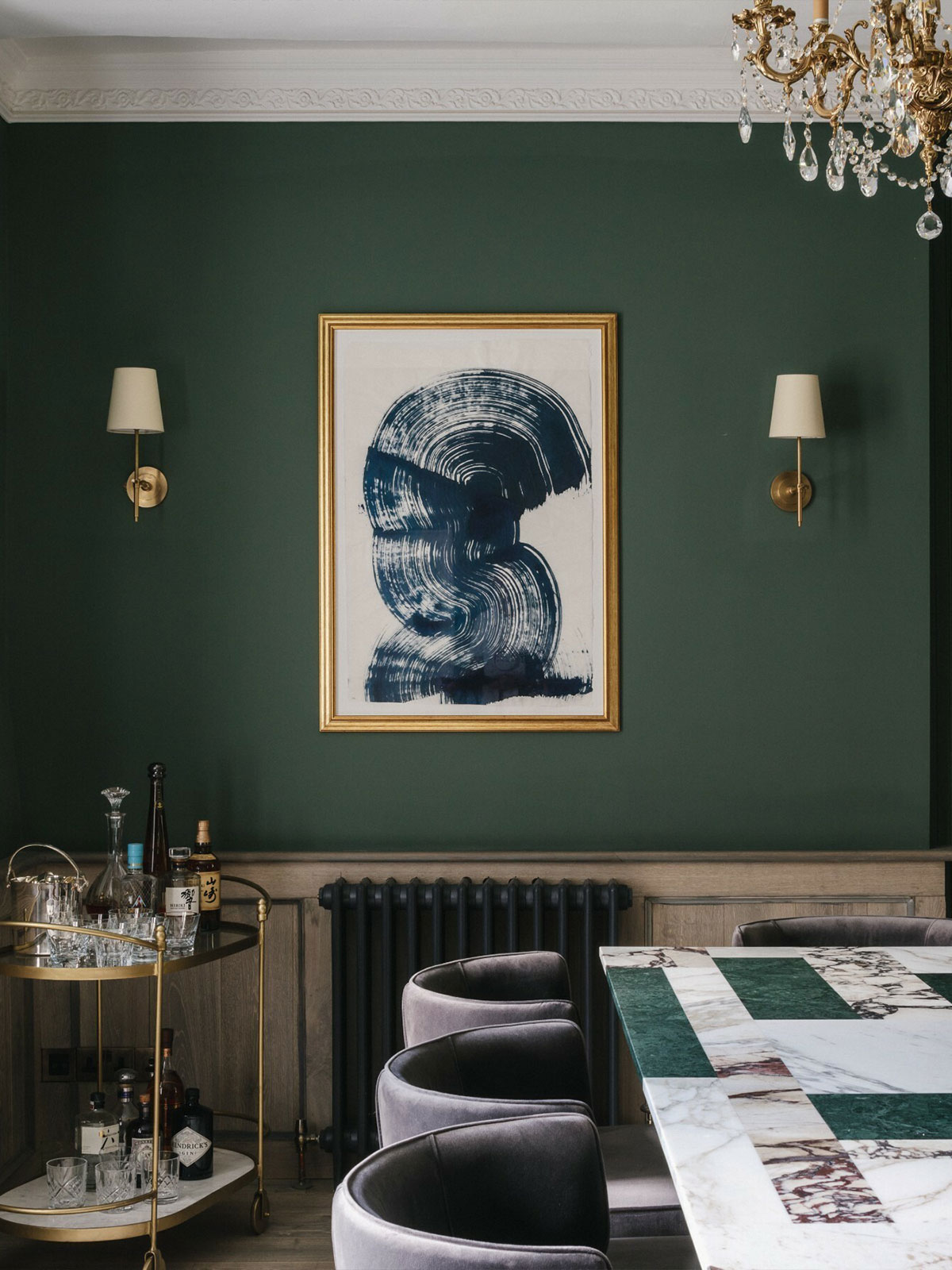 Elegant dining room with deep green walls, gold-framed artwork, and marble-topped table.