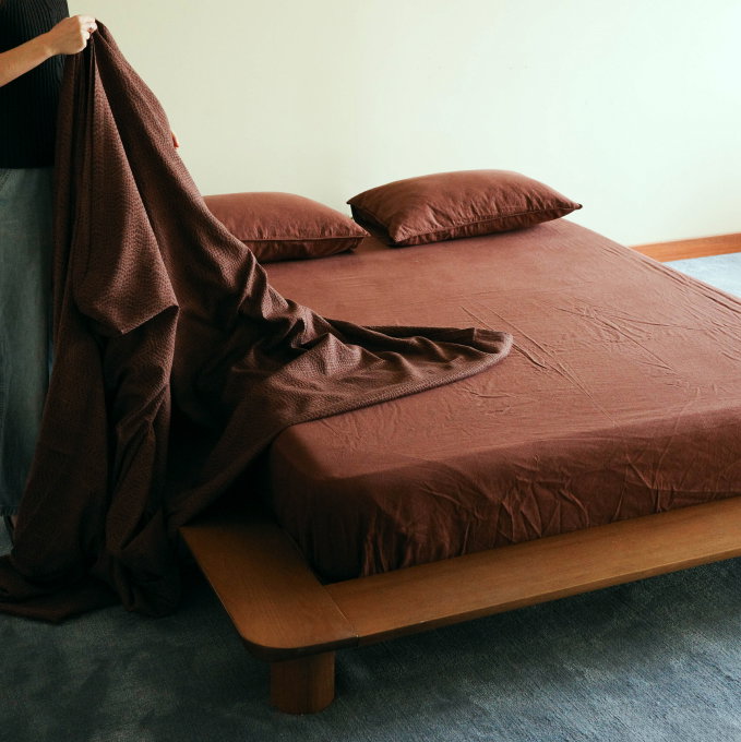 Person holding maroon blanket over a bed