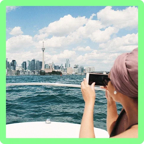 Image description: A woman taking a picture of the Toronto skyline from a boat