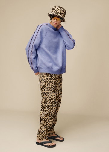 A studio shot of a model in a leopard print hat and trousers, a crew-neck jumper and the Seaside Ii Flip Flops