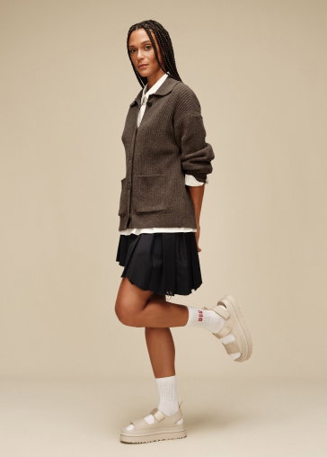 A studio shot of a model wearing a cardigan, skirt and the GoldenGlow Sandals