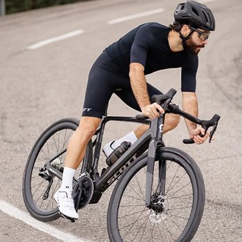Cyclist in black kit and helmet leaning into a turn on a Scott road bike on a tarmac road