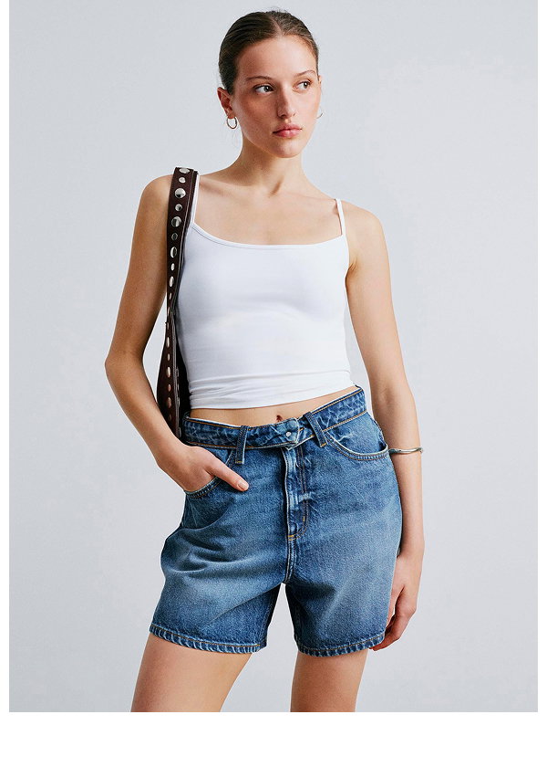 Woman wearing white cropped tank and denim shorts with black bag