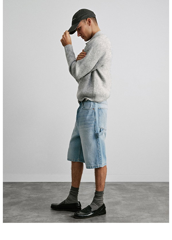 Man wearing gray sweater, denim shorts, and black socks with loafers
