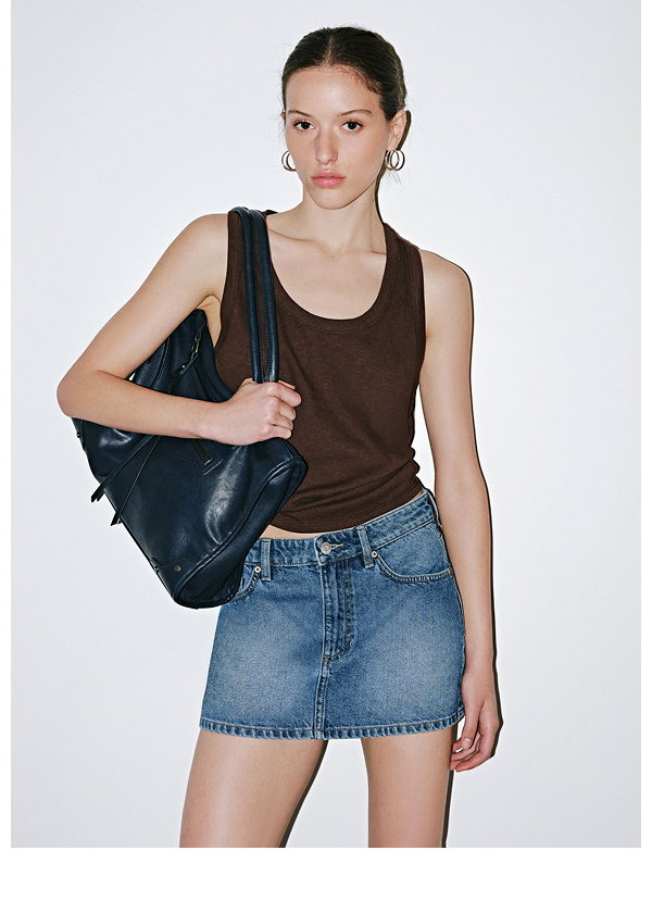 Woman wearing brown tank top, denim skirt, and navy shoulder bag