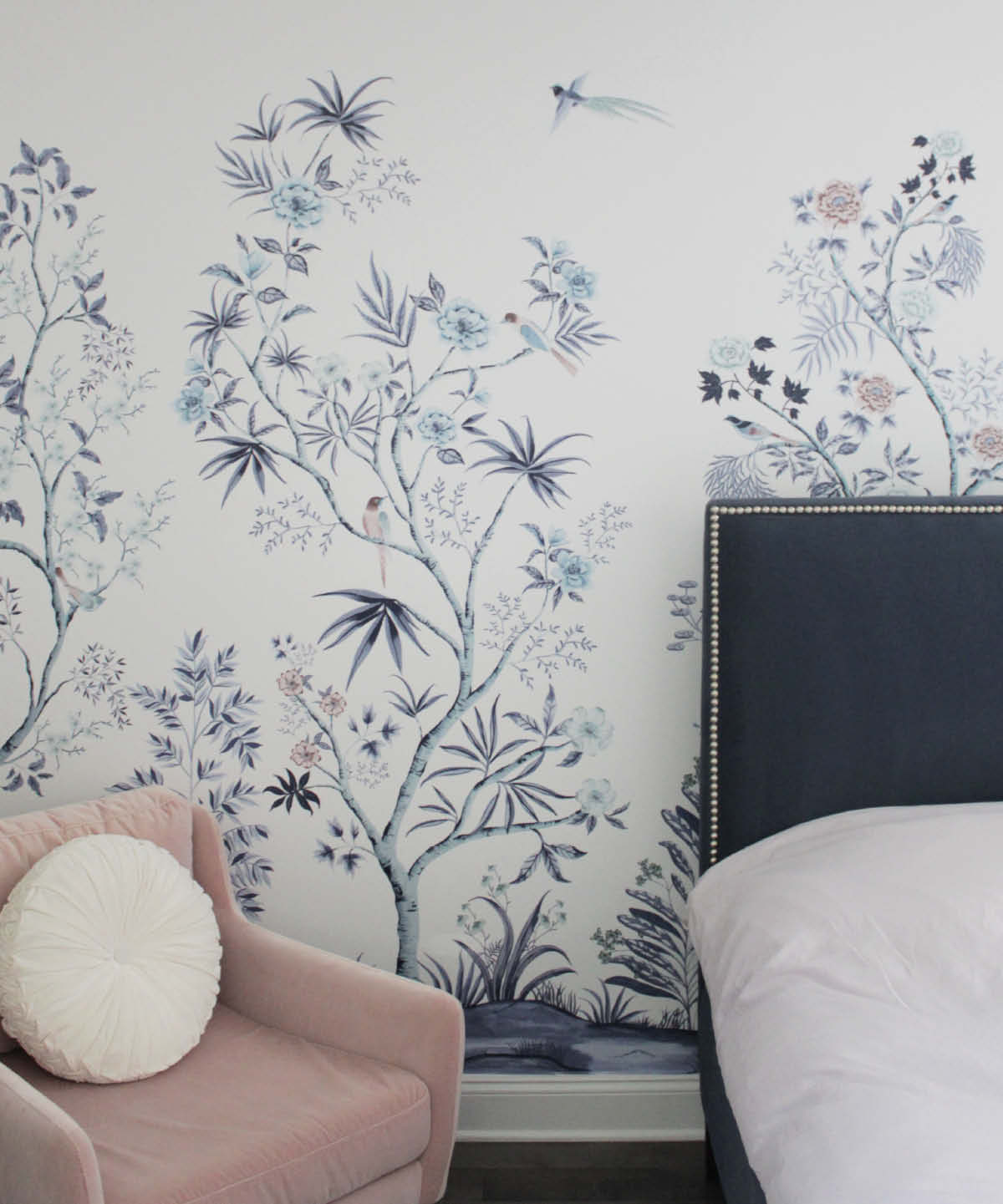 Image of Tempaper's Fancy Tail wall mural on a bedroom wall. A pink chair with a white pillow is shown and part of a bed with a blue headboard.