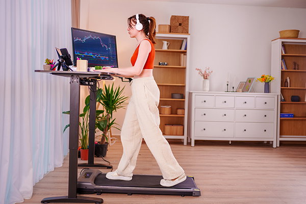 A woman working at a standing desk while walking on a treadmill.
