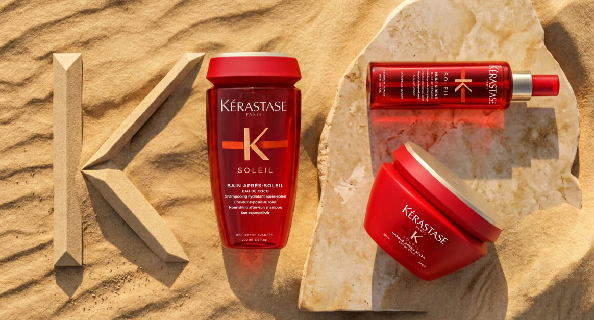 Tre prodotti Kérastase Soleil rossi — shampoo, spray e maschera su sabbia dorata con logo K in rilievo