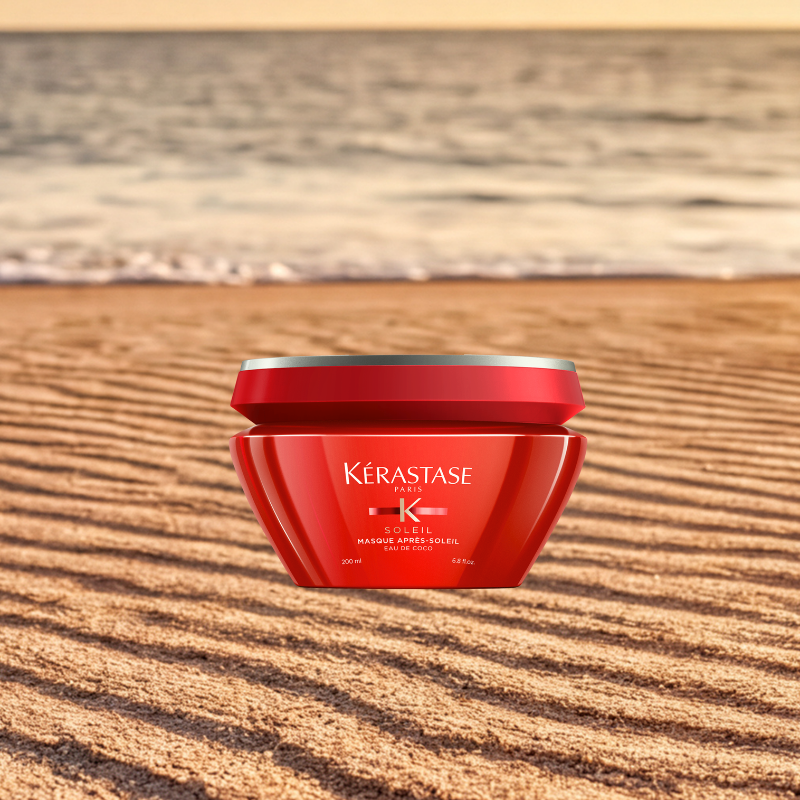 Vasetto rosso Kérastase Soleil Masque Après-Soleil sulla sabbia con mare sullo sfondo