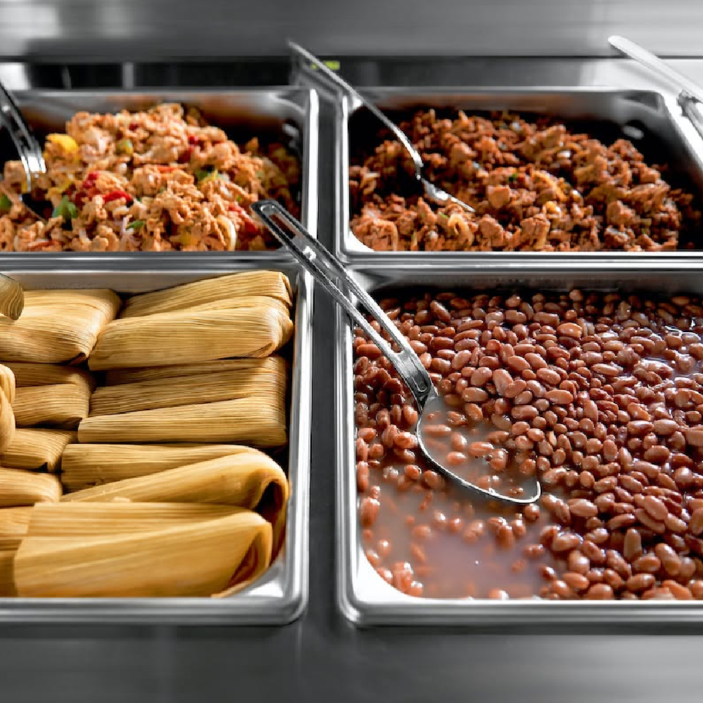 ServeWell steam table holding tamales, pinto beans, seasoned meats, and vegetables in stainless steel food pans for self‑serve or cafeteria service.